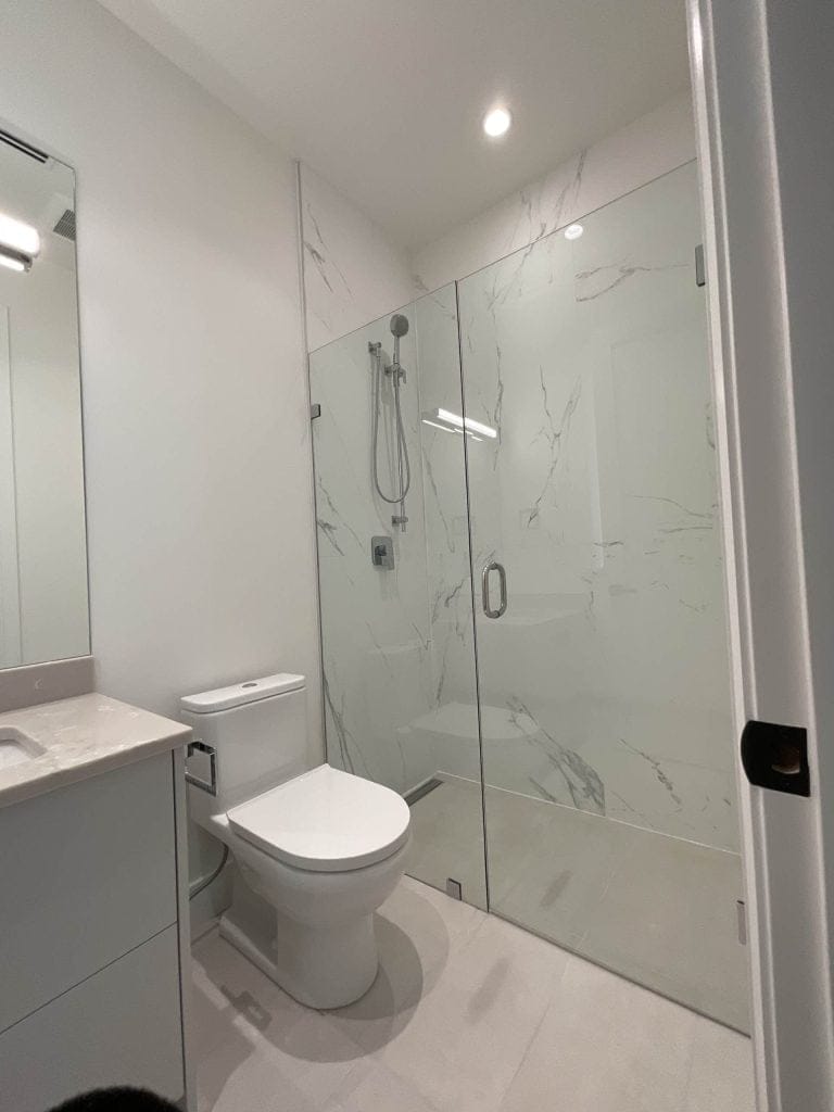 Glass stand shower in the corner with a toldet on the side